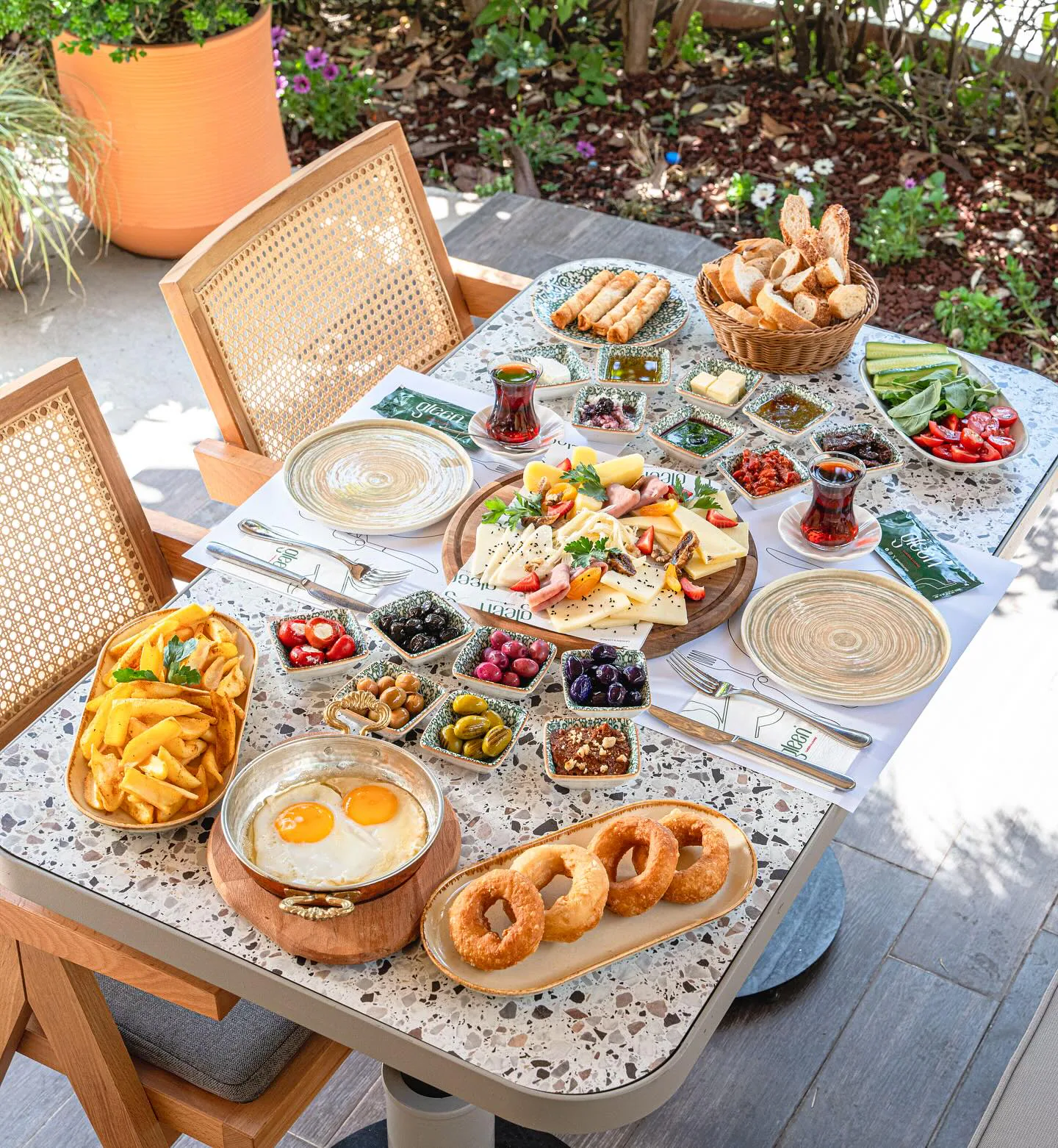 Bahçede, rattan sandalyeler arasında serpme kahvaltı sofrası